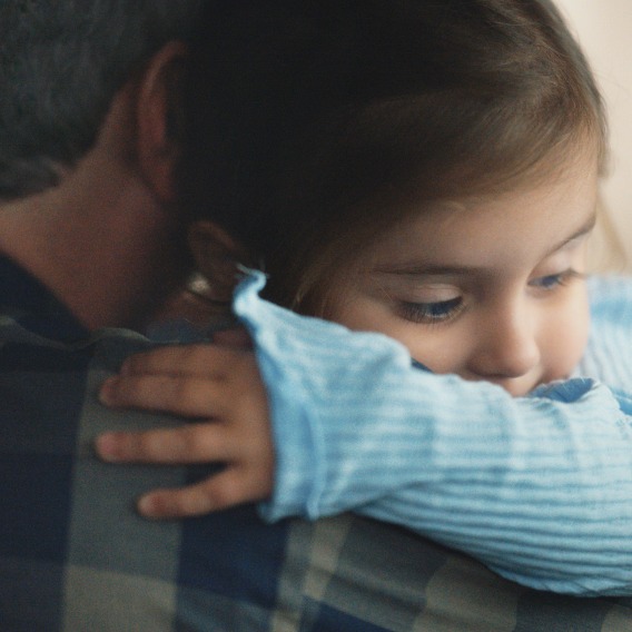 A young kid in a blue sweater hugs her father.